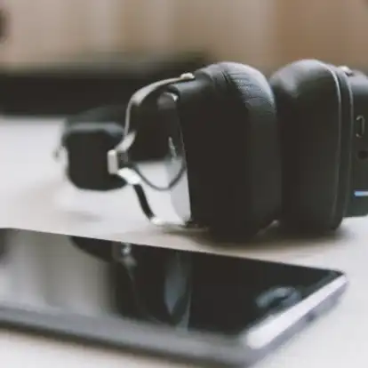 Square black over ear closed wireless headphones and a mobile phone on a table