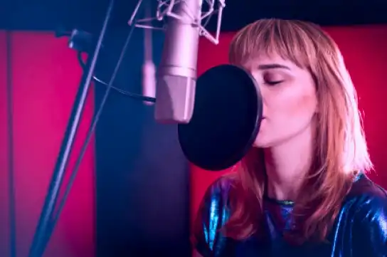 Girl in a studio recording booth singing in the mic through a pop filter sing